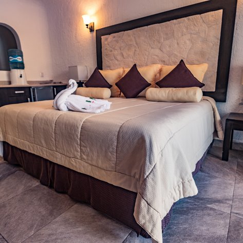 Ein gemütliches Hotelzimmer mit einem großen Bett, dekoriert mit Kissen und einem kunstvoll gefalteten Handtuch auf der Bettdecke.