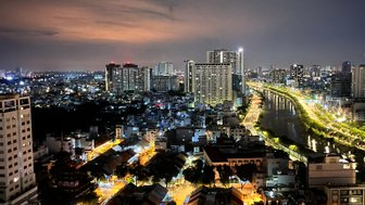 Ein nächtlicher Blick auf die beleuchteten Straßen von Saigon, mit Hochhäusern und einem ruhigen Fluss im Hintergrund.