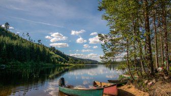 Ein ruhiger See umgeben von dichten Wäldern, mit bunten Kanus am Ufer, die auf das glitzernde Wasser blicken.