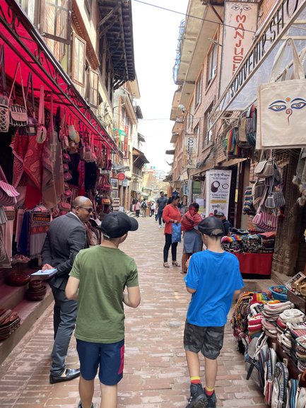 Zwei Jungen gehen durch eine belebte Gasse, umgeben von bunten Souvenirläden und Handwerksständen.