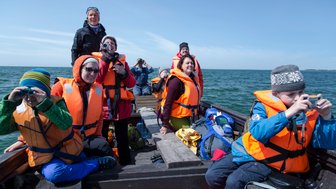 Eine Gruppe von Menschen in orangefarbenen Schwimmwesten genießt eine Bootstour auf dem Wasser, voller Freude und Neugier.