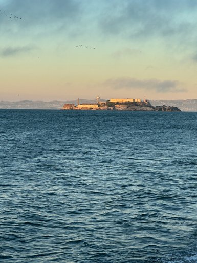 Alcatraz Island erhebt sich majestätisch aus dem glitzernden Wasser, umgeben von sanften Wellen und einem klaren Himmel.