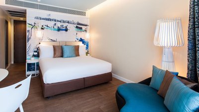 Ein modernes Hotelzimmer mit einem großen Kingsizebett, bunten Kissen und einer stilvollen Lampe im Hintergrund.