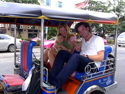 Eine Familie sitzt fröhlich in einem bunten Tuk-Tuk, umgeben von städtischem Verkehr und lebhaften Farben.