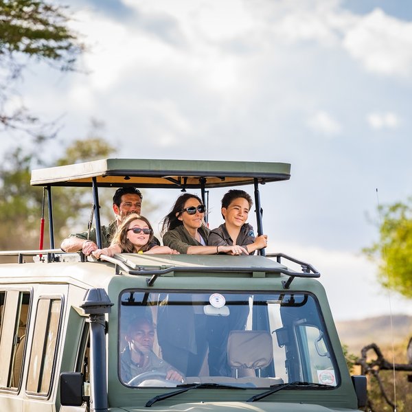 Familie erkundet mit Guide die Tierwelt in einem Safarijeep – Tansania mit Kindern