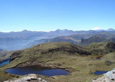 Eine atemberaubende Berglandschaft mit sanften Hügeln und glitzernden Seen unter einem strahlend blauen Himmel.