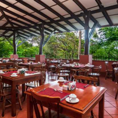 Ein einladendes Restaurant mit Holztischen und Stühlen, umgeben von üppigem Grün und einem offenen Dach.