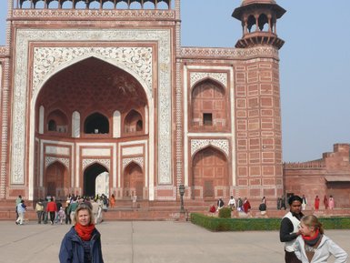 Eine Frau steht vor dem beeindruckenden Taj Mahal, während andere Besucher im Hintergrund die Architektur bewundern.
