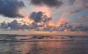 Ein atemberaubender Sonnenuntergang über dem Meer, mit leuchtenden Farben und dramatischen Wolkenformationen am Himmel.