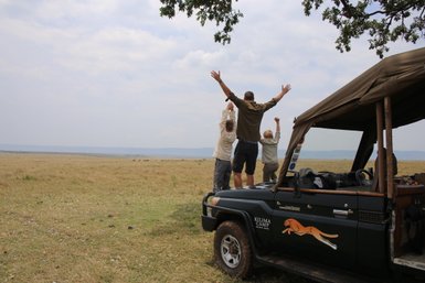 Eine Gruppe von Menschen steht auf einem Geländewagen und genießt die Aussicht auf die weite Savanne unter einem bewölkten Himmel.