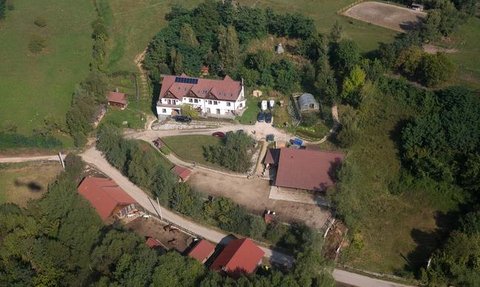 Eine Luftaufnahme zeigt ein weitläufiges Gelände mit einem großen, weißen Gebäude und mehreren roten Dächern in der Umgebung.