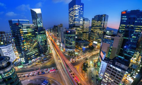 Die Stadt Seoul erstrahlt in der Dämmerung, mit leuchtenden Wolkenkratzern und lebhaften Straßen voller Autos.