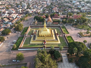 Ein goldener Stupa erhebt sich majestätisch über die Stadt Vientiane, umgeben von grünen Gärten und historischen Gebäuden.