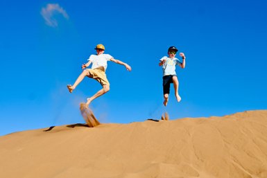 Kinder genießen die Freiheit und springen voller Freude auf den weiten Sanddünen der Wüste – Marokko Reise mit Kindern