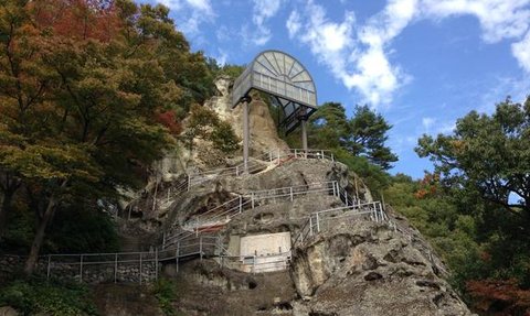 Eine steile Felswand mit einem modernen Aussichtspunkt, umgeben von buntem Herbstlaub und klarem Himmel.