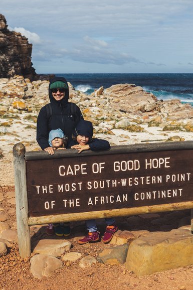 Eine Mutter steht mit zwei Kindern vor dem Schild am Kap der Guten Hoffnung, das den südwestlichsten Punkt Afrikas markiert.