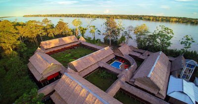 Eine Luftaufnahme eines rustikalen Resorts mit Strohdächern, umgeben von üppigem Grün und einem ruhigen Fluss im Hintergrund.