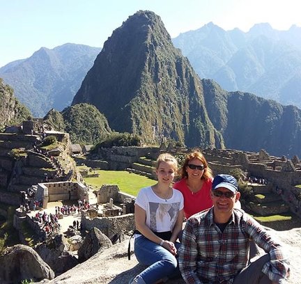 Eine Familie posiert fröhlich vor der beeindruckenden Kulisse von Machu Picchu, umgeben von majestätischen Bergen.