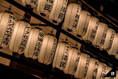 Eine Reihe von traditionellen japanischen Laternen leuchtet sanft in der Dunkelheit, mit kunstvollen Schriftzeichen darauf.