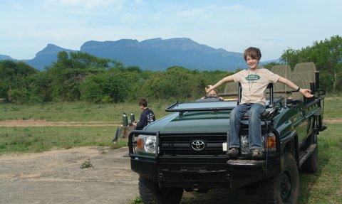 Fröhliches Kind im Safari-Fahrzeug während einer Pirschfahrt durch die Savanne – Südafrika mit Kindern