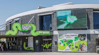 Das moderne Gebäude des Skyline Luge in Busan zeigt eine lebendige grüne Fassade und zahlreiche Besucher an der Kasse.