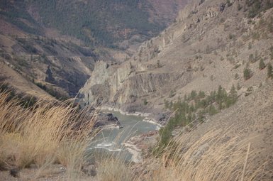 Ein Blick auf den Fraser Canyon, wo der Fluss zwischen steilen, felsigen Ufern fließt, umgeben von kargem Gelände.