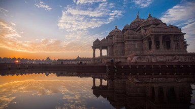 Das beeindruckende Akshardham-Tempelgebäude spiegelt sich majestätisch im ruhigen Wasser bei Sonnenaufgang wider.
