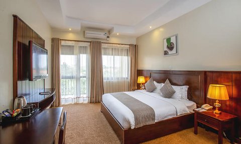 Ein elegantes Hotelzimmer mit einem großen Bett, einem Fernseher und einem Balkon, der viel Tageslicht hereinlässt.