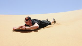 Ein Mann rutscht mit dem Bauch auf einer Matte eine Düne hinunter - Namibia Rundreise mit Kindern