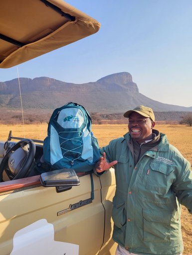 Ein freundlicher Guide steht neben einem For Family Reisen-Rucksack und lacht in die Kamera – Südafrika mit Kindern