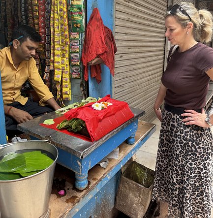 Eine Frau mit einem Leopardenrock betrachtet neugierig ein rotes Tuch mit Blumen auf einem Tisch in einem indischen Straßenladen.