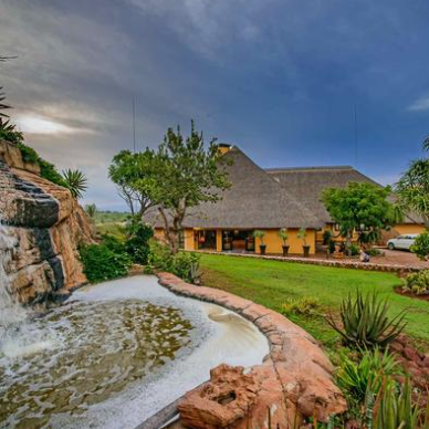 Eine malerische Lodge mit einem Wasserfall und üppigem Grün, umgeben von tropischen Pflanzen und einem bewölkten Himmel.