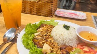 Ein Teller mit gegrilltem Hähnchen, Reis und frischem Gemüse, serviert in einem lebhaften Restaurant mit Motorrädern im Hintergrund.