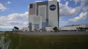 Das NASA-Gebäude mit der amerikanischen Flagge und dem NASA-Logo steht unter einem klaren Himmel mit einigen Wolken.
