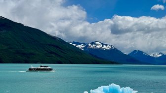 Ein modernes Boot fährt über das türkisfarbene Wasser, umgeben von majestätischen Bergen und schneebedeckten Gipfeln.