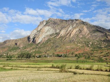 Eine beeindruckende Berglandschaft mit steilen Felsen und üppigen Wiesen unter einem strahlend blauen Himmel.