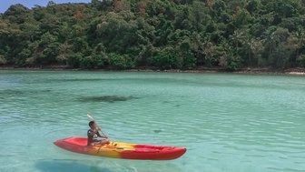 Erwachsener fährt in Kanu über kristallklares Wasser auf Inselparadies Koh Talu - Thailand mit Kindern