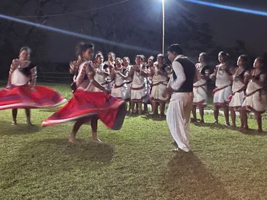 Zwei Tänzerinnen in traditionellen Kleidern drehen sich fröhlich, während eine Gruppe von Zuschauern sie anfeuert.