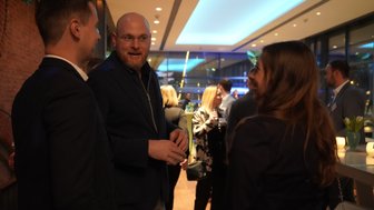 Drei Personen unterhalten sich in einem modernen, stilvollen Raum mit sanfter Beleuchtung und einer entspannten Atmosphäre.