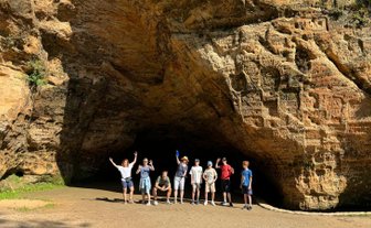 Eine Gruppe von sieben Personen posiert fröhlich vor einer beeindruckenden Felswand im Gauja-Nationalpark.