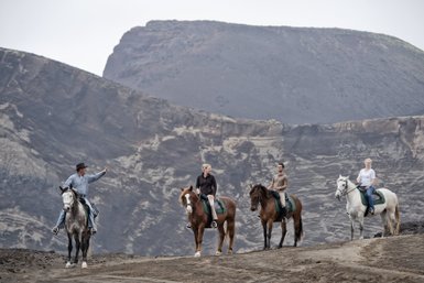 Eine Gruppe von Reitern auf Pferden steht vor einer beeindruckenden, zerklüfteten Berglandschaft.