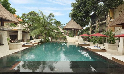 Ein ruhiger Poolbereich in Bali, umgeben von tropischen Pflanzen und Sonnenliegen unter roten Sonnenschirmen.