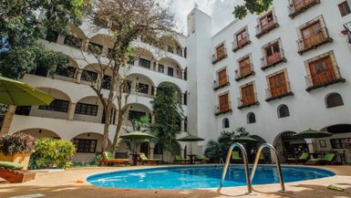 Ein einladender Innenhof mit einem blauen Pool, umgeben von üppigem Grün und gemütlichen Liegen unter Sonnenschirmen.