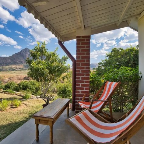 Eine Terrasse mit zwei Liegestühlen in orange-weißen Streifen, umgeben von üppigem Grün und Blick auf majestätische Berge.