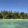 Tropische Insel mit üppiger Vegetation, umgeben von klarem, grünem Wasser unter einem strahlend blauen Himmel.