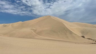 Eine weite Sanddüne erstreckt sich unter einem strahlend blauen Himmel mit einigen Wolken, die sanft vorbeiziehen.