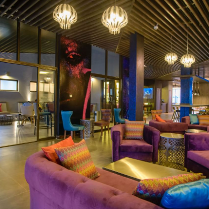 Ein stilvolles Café mit lila Sofas und bunten Kissen, das eine einladende Atmosphäre für Gäste schafft.
