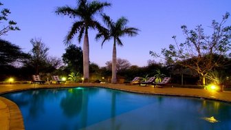 Ein ruhiger Pool in der Dämmerung, umgeben von Palmen und sanftem Licht, das eine entspannende Atmosphäre schafft.