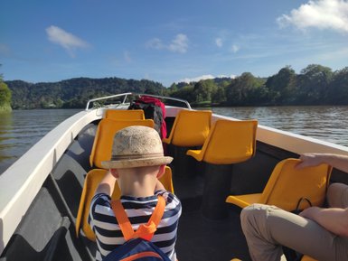 Kleinkind sitzt neugierig im Boot während einer Flusssafari auf dem Kinabatangan-Fluss – Malaysia & Borneo Reise mit Kindern
