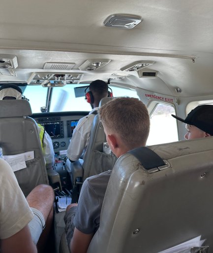Im Inneren eines Kleinflugzeugs sitzen Passagiere, während der Pilot die Instrumente steuert und die Aussicht genießt.